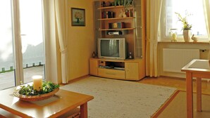 A living room with a television, bookshelf, and a window with curtains. - Ferienwohnung Lehmann 58 qm, Erdgeschoss, mit Terrasse und Separatem Schlafzimmer (Bad Endorf)