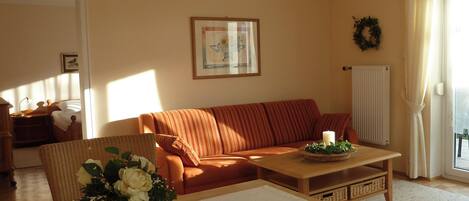 A living room with a sofa, a coffee table, a vase with flowers, a framed picture on the wall, and a window with curtains.