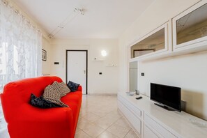 Un salon avec un canapé rouge, un téléviseur à écran plat et un meuble de rangement blanc.