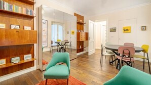 A room with a wooden bookshelf, a dining table with chairs, and a mirror reflecting the room. - GuestHost - Corso Vittorio Central & Roomy Flat x4 (Torino)