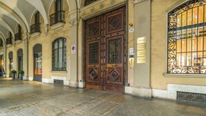A spacious hallway with a large ornate wooden door, a sign with a number, and a window with decorative iron bars. - GuestHost - Corso Vittorio Central & Roomy Flat x4 (Torino)
