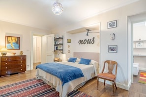 A bedroom with a bed, dresser, chair, and a wall with the word 'nous' and framed pictures.