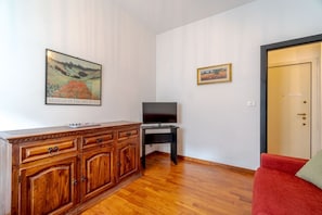 A room with a wooden cabinet, a television on a stand, a red sofa, and two framed artworks on the wall.