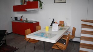 A compact kitchen with a microwave, sink, and red cabinetry. A dining table with chairs and a map is in the center. - GuestHost - San Martino / Gaslini Urban Loft x4 (Genova)