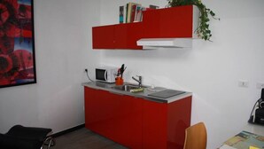 A compact kitchen with a microwave, sink, and red cabinetry. - GuestHost - San Martino / Gaslini Urban Loft x4 (Genova)