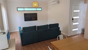 Ein modernes Wohnzimmer mit einem dunkelgrünen Sofa, einem Flachbildfernseher, einer Deckenleuchte und Holzboden.