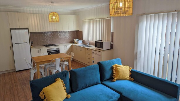 A compact living space with a kitchenette, a dining area, and a sofa with yellow cushions. - 1 bedroom guesthouse near airport with private access and parking (Arncliffe)