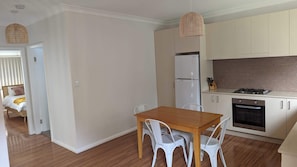 Eine kleine Küche mit weißen Schränken, einem Kühlschrank, einem Herd und einem Essbereich mit einem Holztisch und weißen Stühlen.