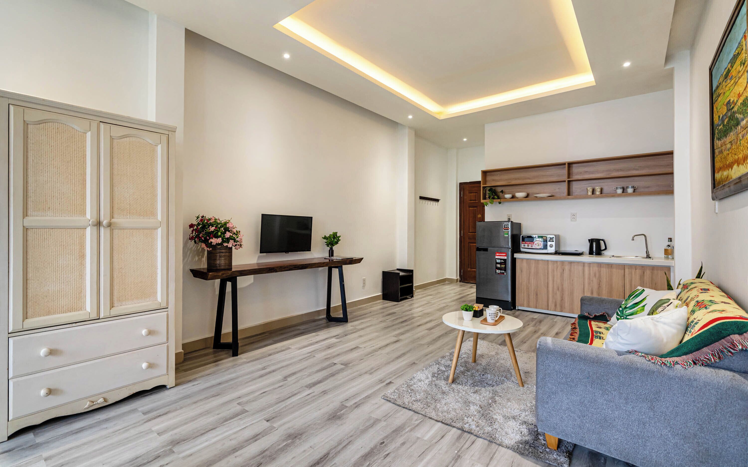 A modern living room with a sofa, a coffee table, a TV, and a kitchen area with a refrigerator and microwave.