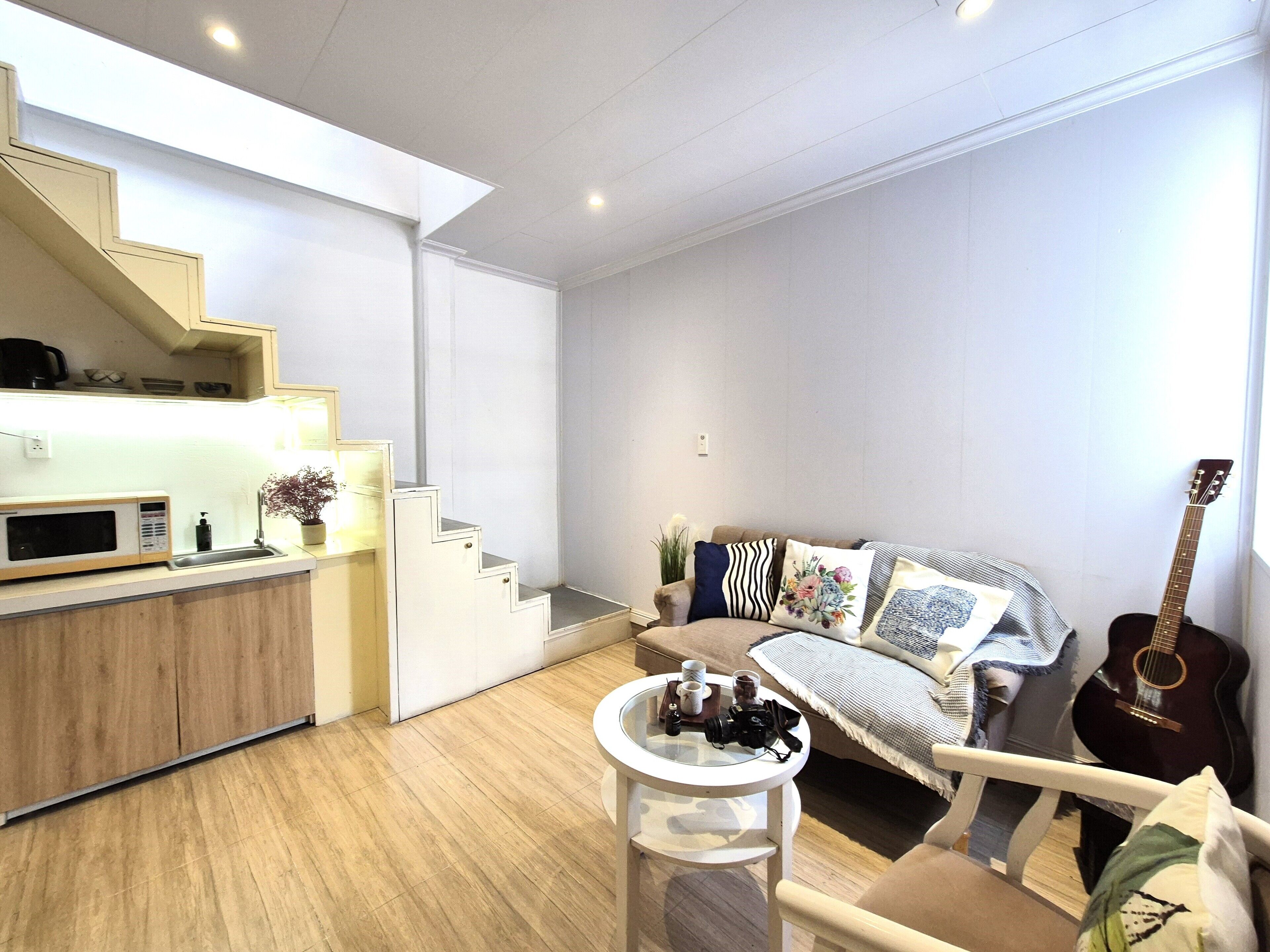 A modern living room with a sofa, a coffee table, a guitar, and a staircase leading to a kitchen area.