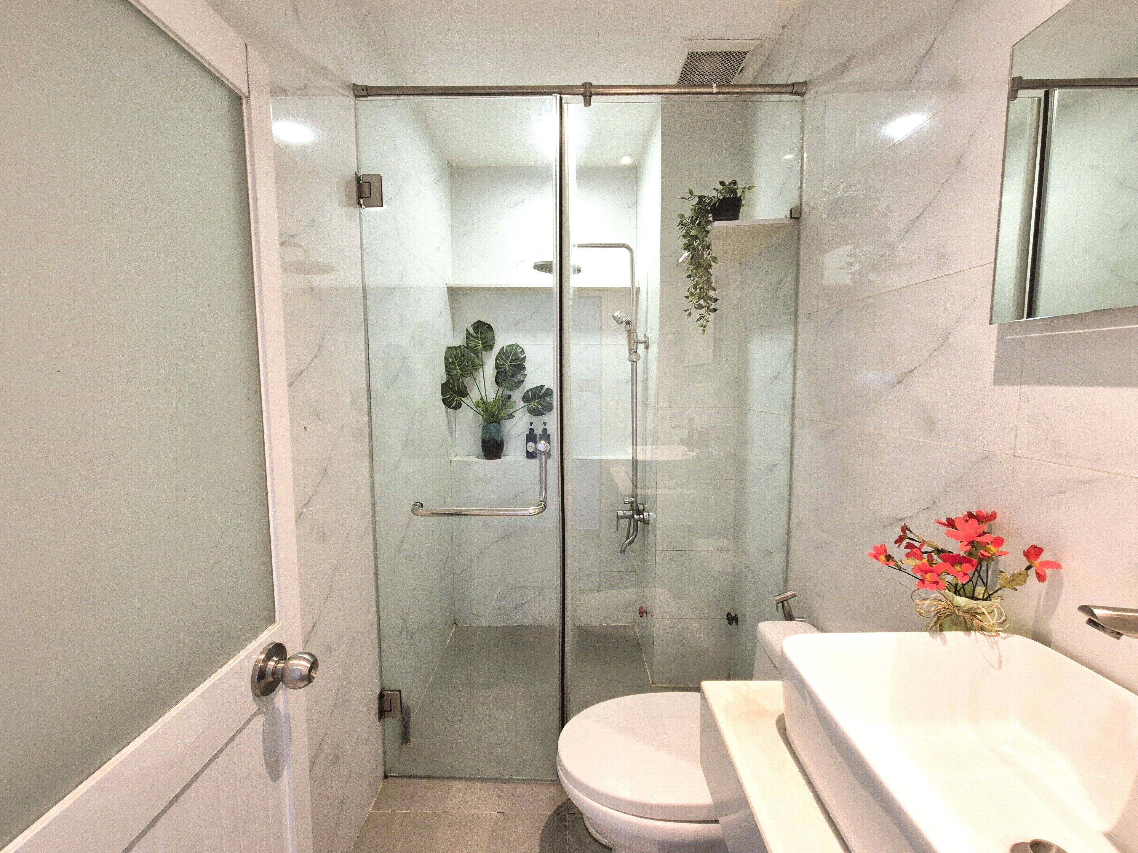 A modern bathroom with a glass-enclosed shower, a white toilet, and a vanity with a mirror.