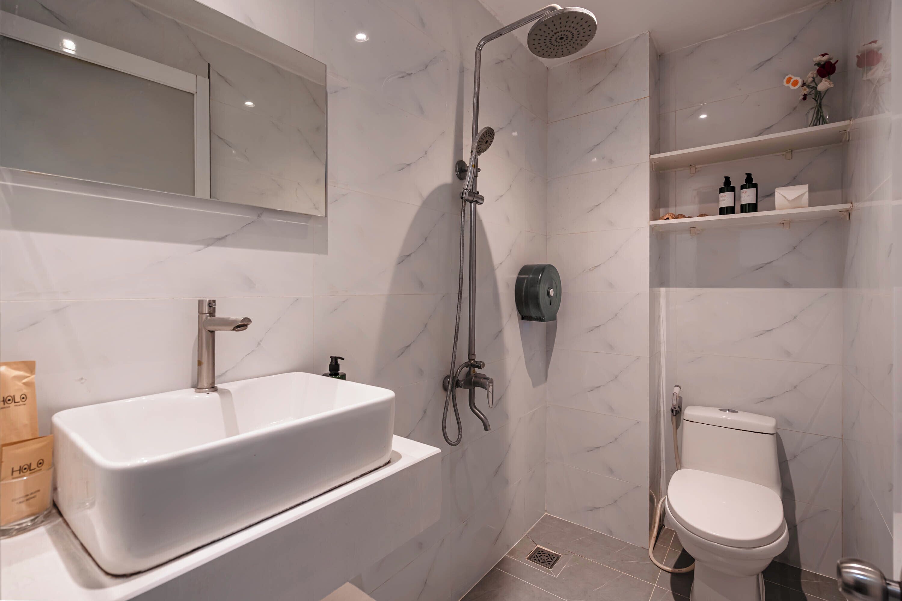 A modern bathroom with a large rectangular sink, a handheld showerhead, a toilet, and marble-patterned walls.
