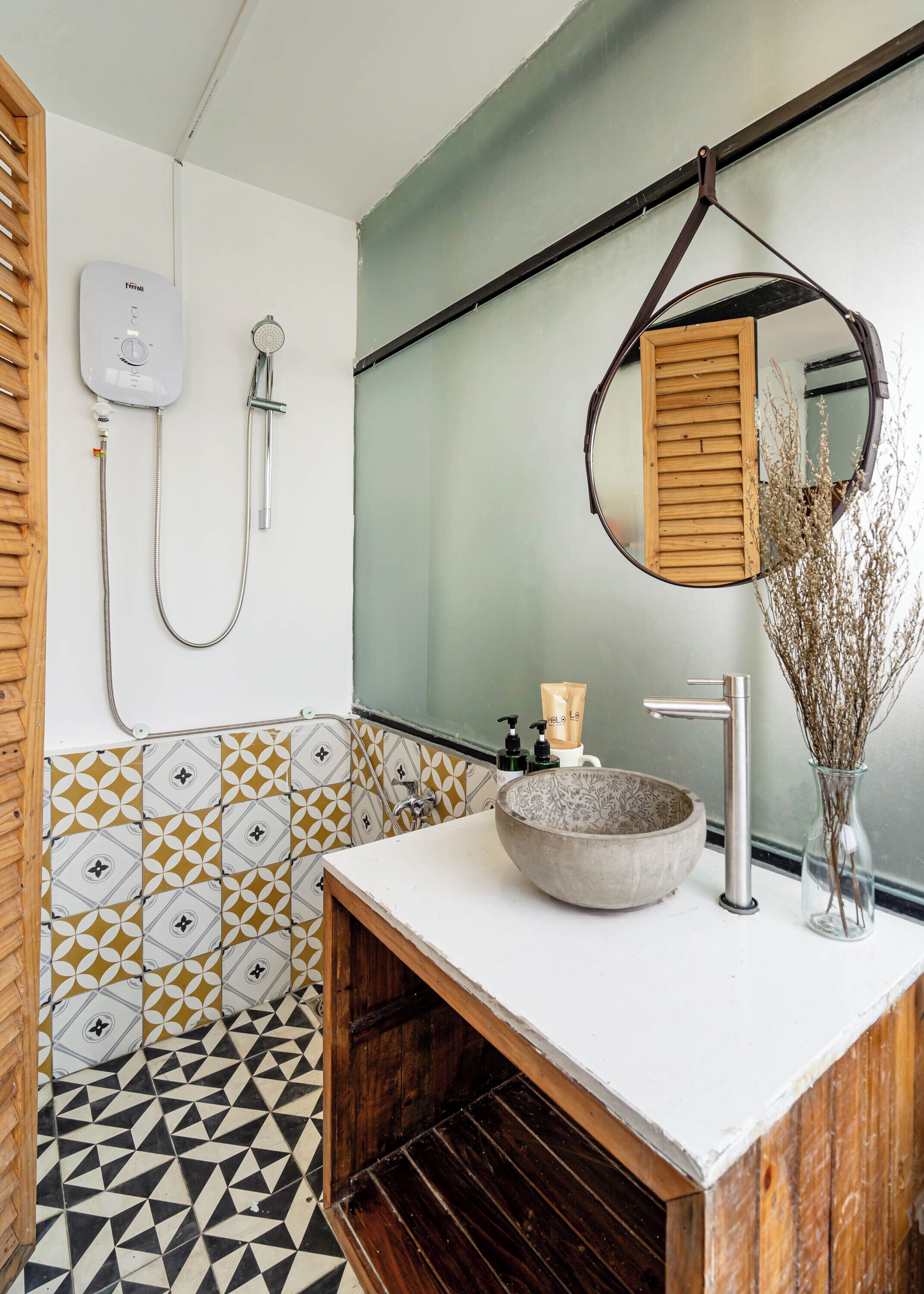 A bathroom with a white sink, a wooden vanity, a large mirror, a shower, and patterned tiles.