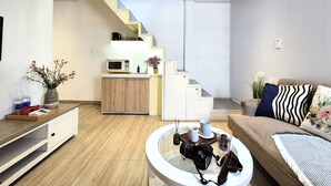 A modern living room with a staircase, a kitchen area, and a seating area with a couch and coffee table. - HoLo Ben Thanh Saigon - Serviced HomeStay (Ho Chi Minh City)
