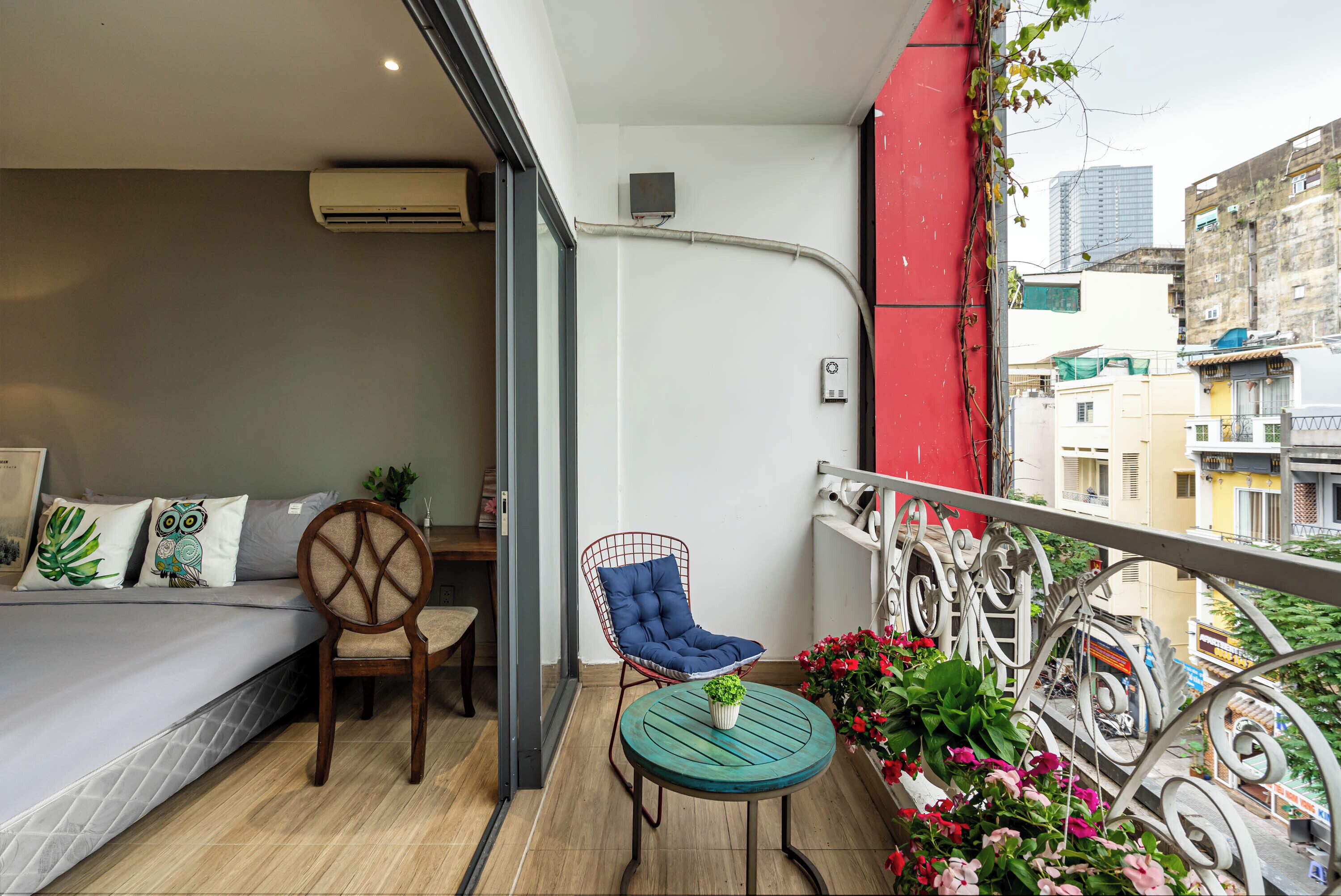 A balcony with a bed, a chair, a small table with a plant, and a railing with flowers.