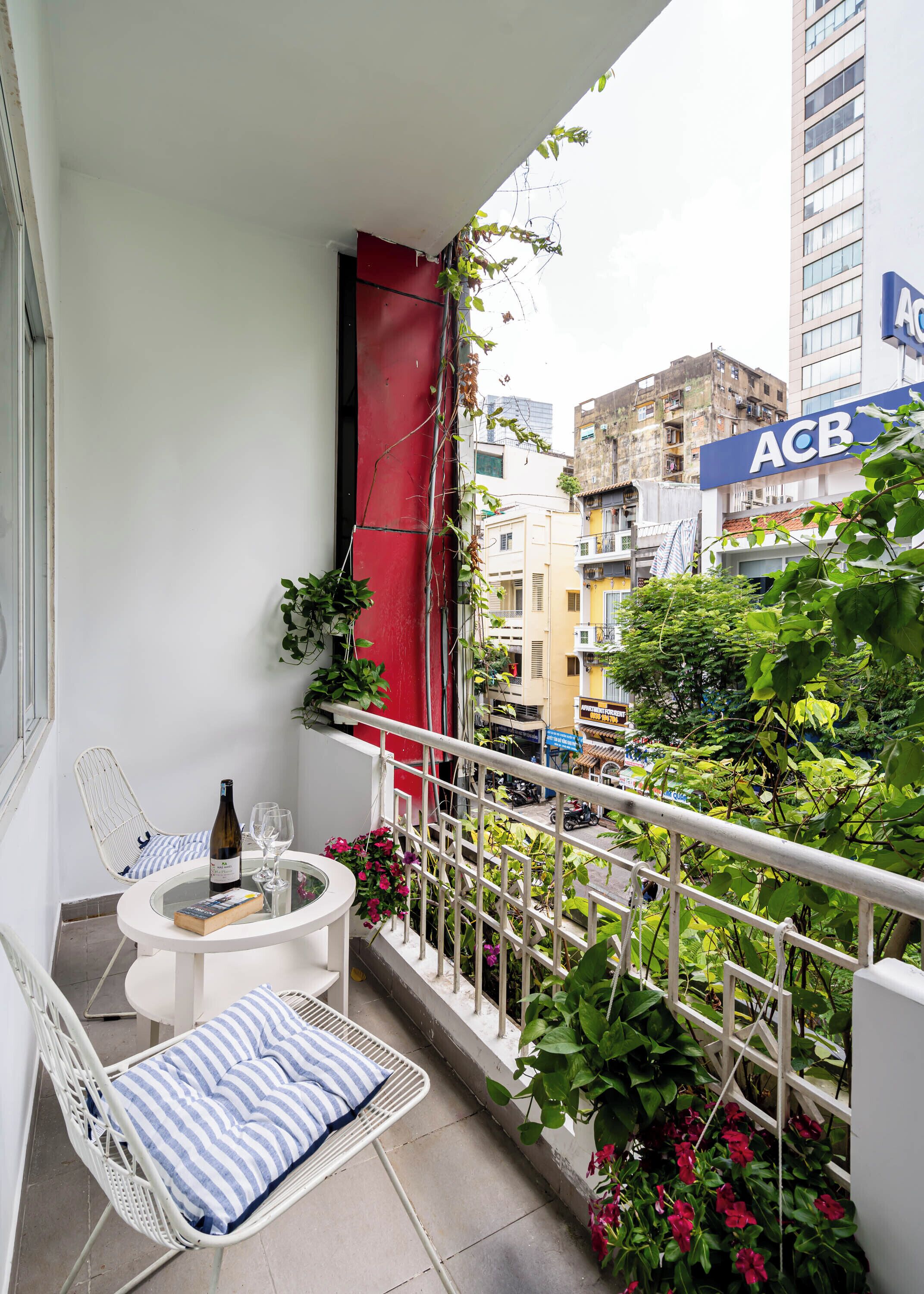 A balcony with a white chair, a small table, a bottle, and a glass. There are plants and flowers around the balcony.