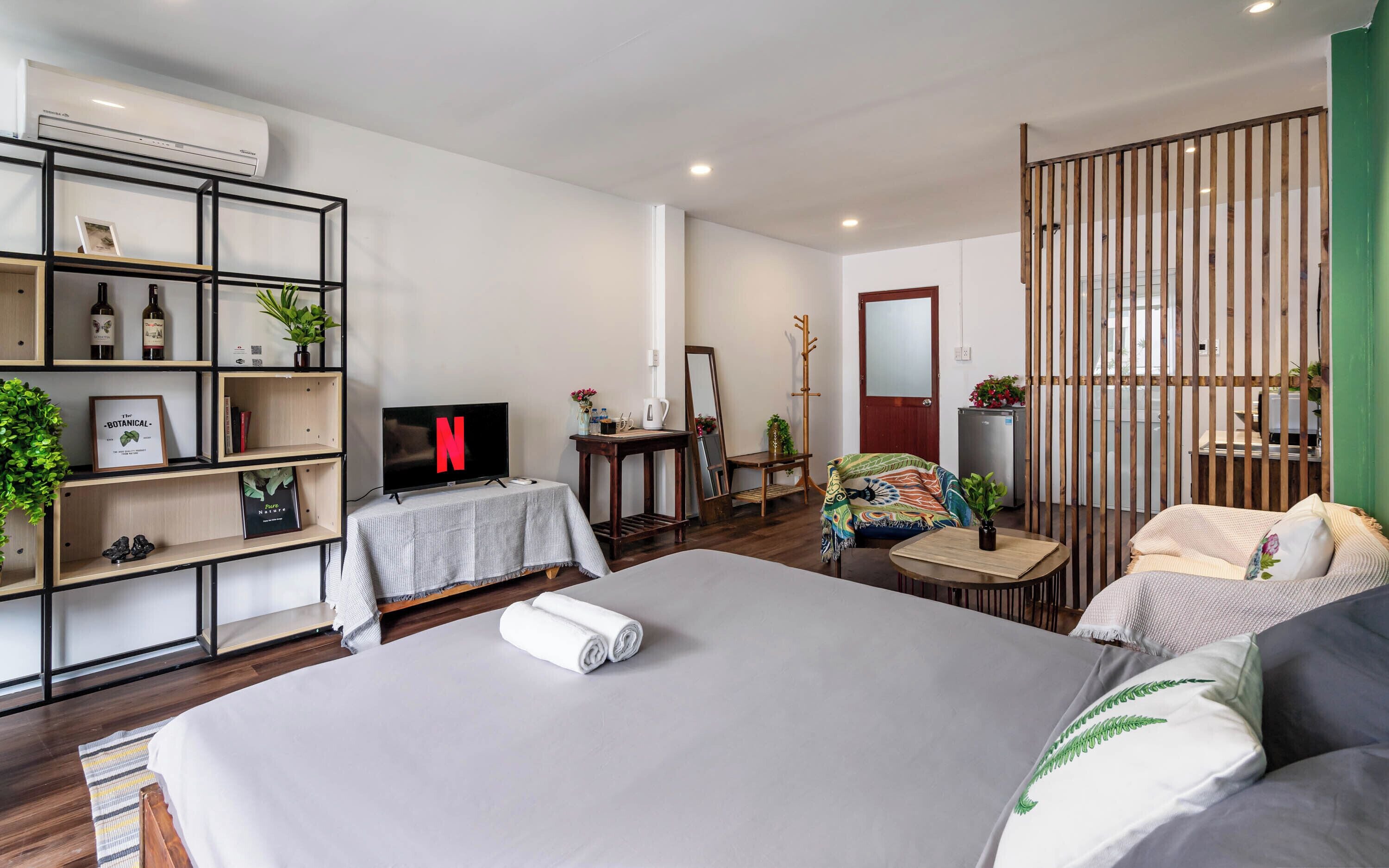 A modern bedroom with a large bed, a TV, a bookshelf, a desk, and a green partition.
