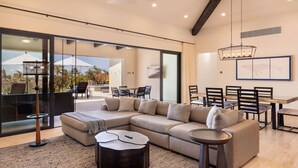 A modern living room with a sectional sofa, a coffee table, and a dining area with chairs and a table. - Luxurious 4BR Casita – Your Perfect Getaway! (Cabo San Lucas)