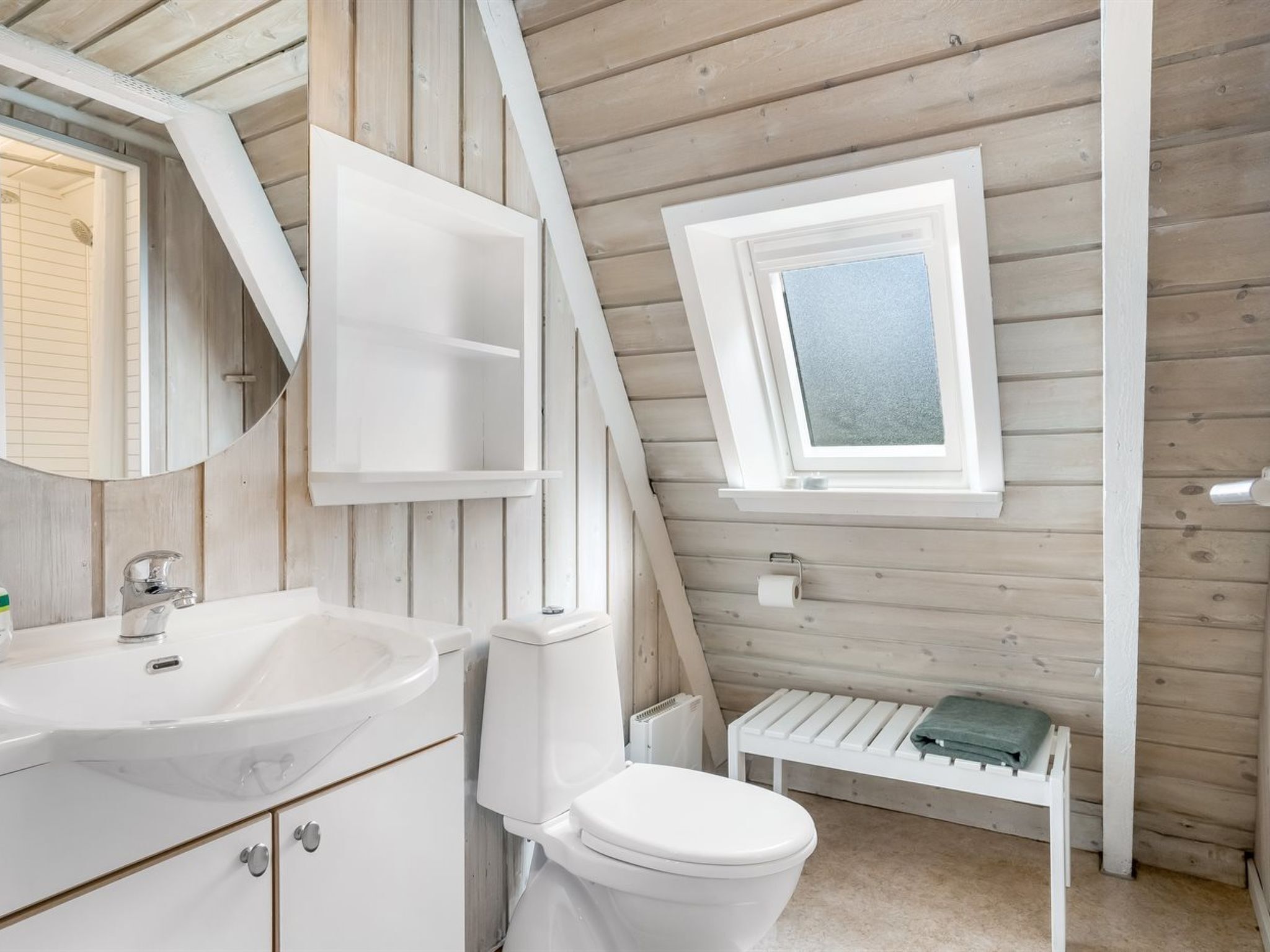 Une salle de bain avec un lavabo blanc, des toilettes et une petite fenêtre.