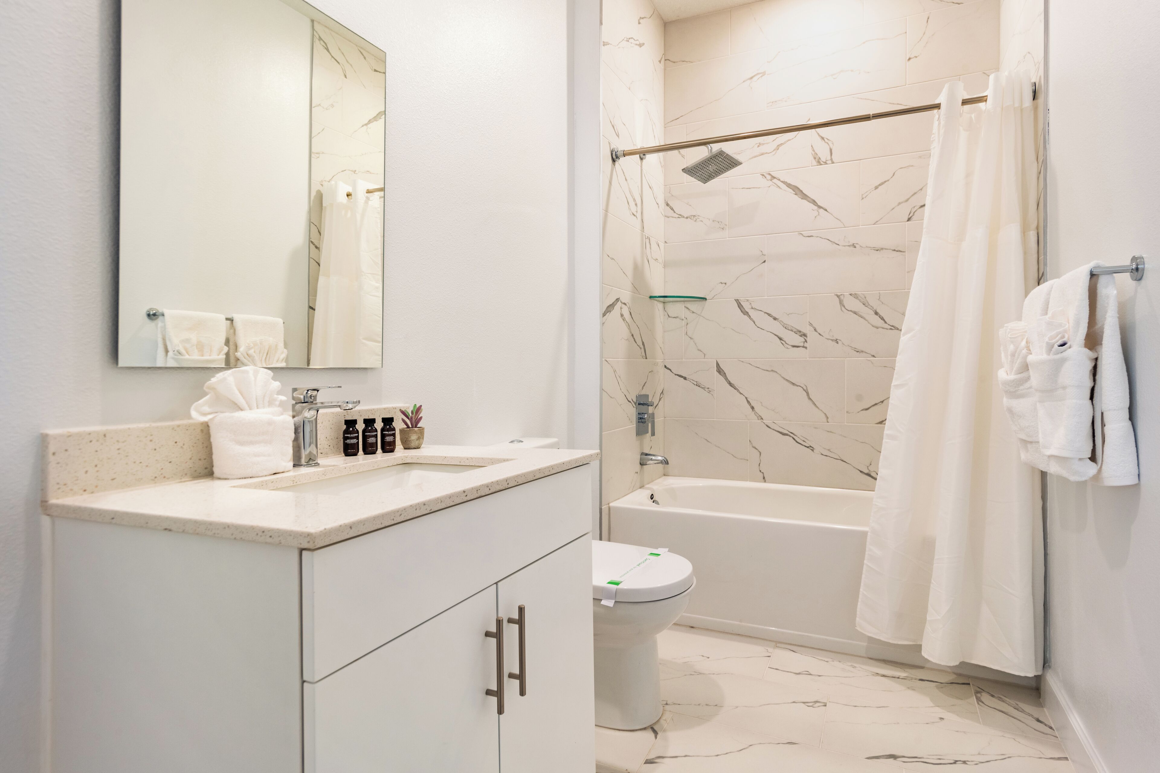 Une salle de bain moderne avec un sol en marbre, une baignoire, des toilettes et un lavabo surmonté d’un miroir.