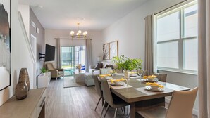 Un espace repas moderne avec une table en bois dressée pour quatre personnes, un canapé et une grande fenêtre agrémentée de rideaux.