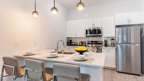 Une cuisine moderne avec des meubles blancs, des appareils en acier inoxydable et un îlot central doté de tabourets de bar.