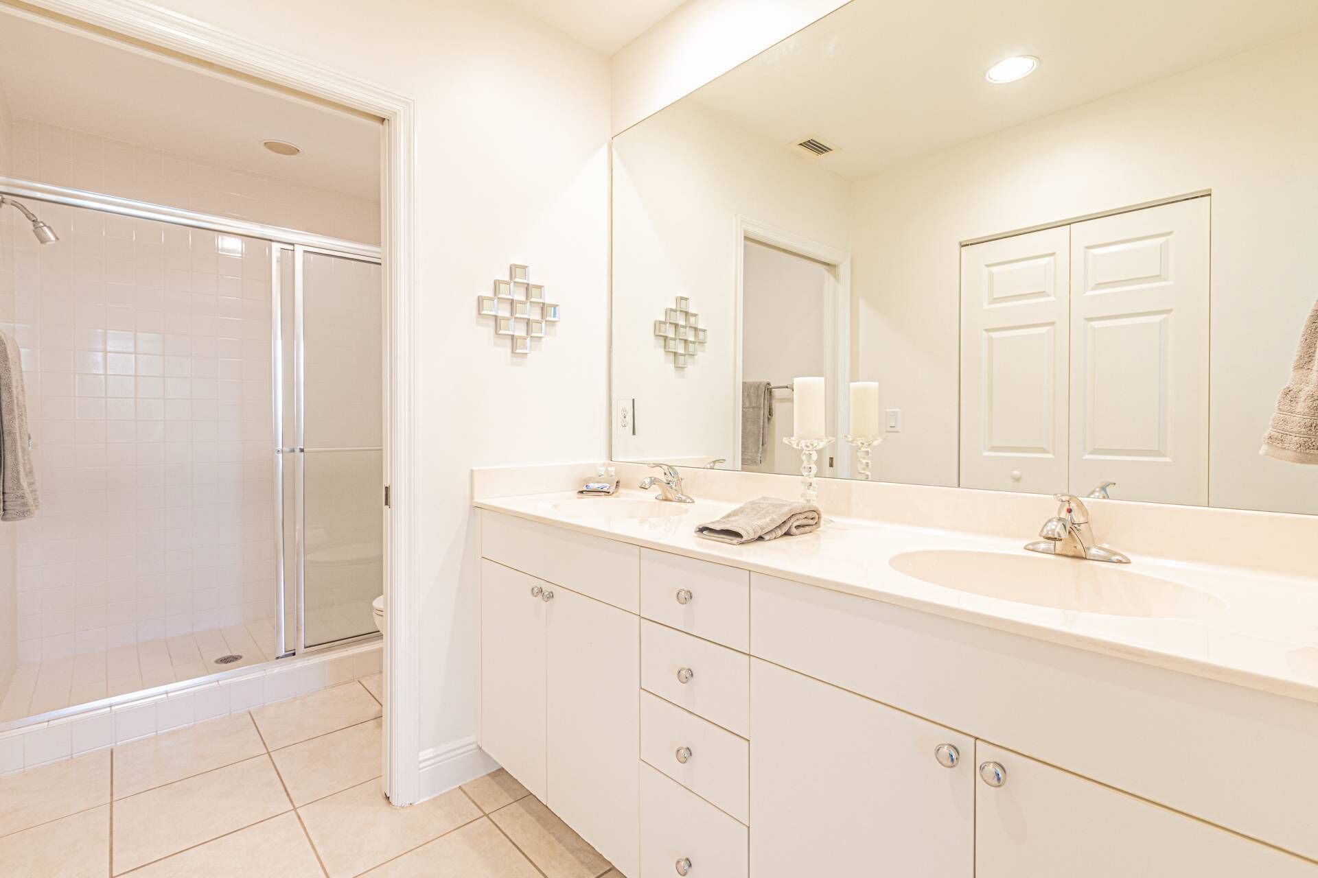 A bathroom with a walk-in shower, a large mirror, and a vanity with a sink and multiple drawers.