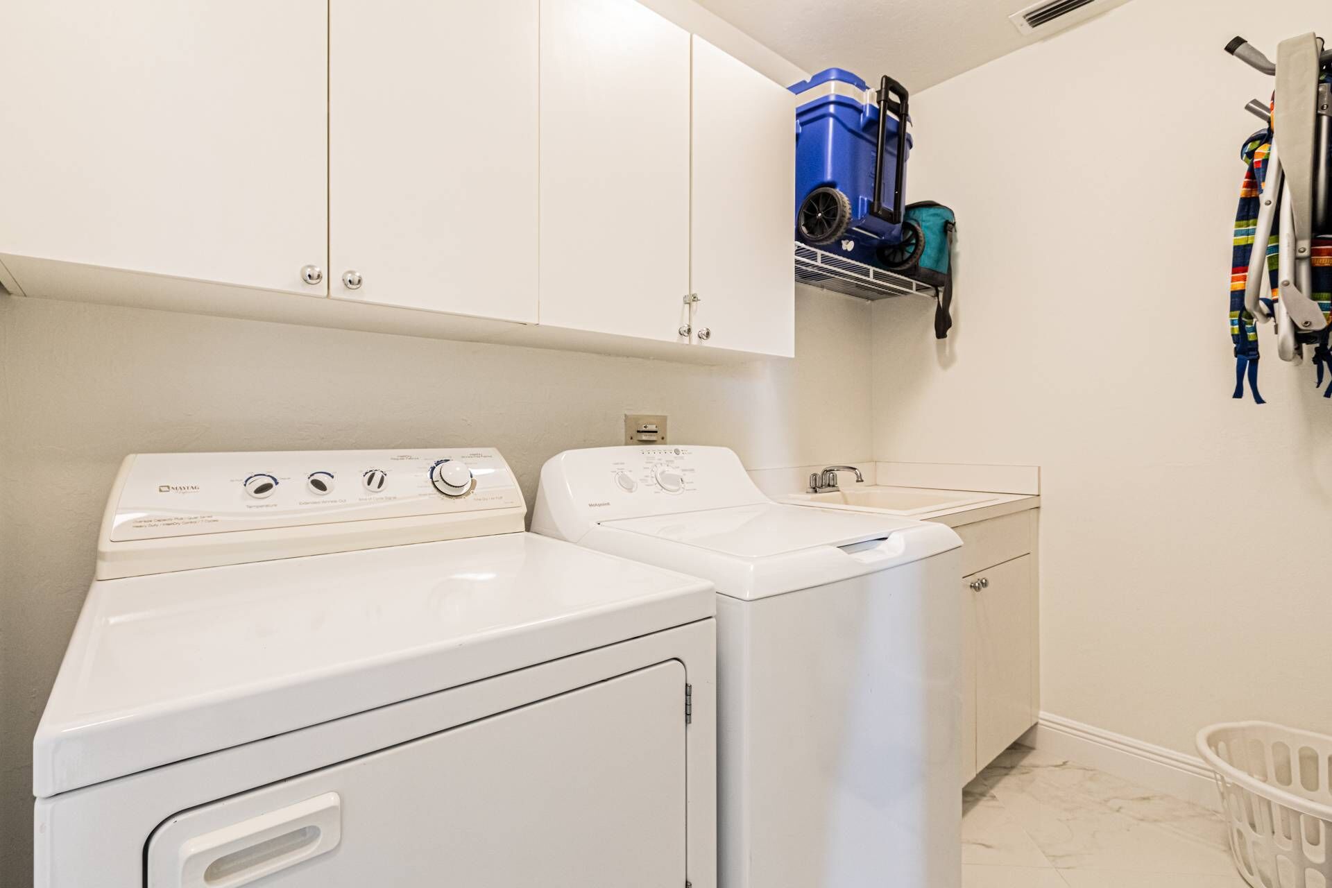 Un espace buanderie comprenant deux machines à laver blanches, un aspirateur bleu et un panier à linge blanc.