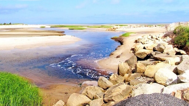 Paisaje costero con playa arenosa, costa rocosa y agua tranquila.