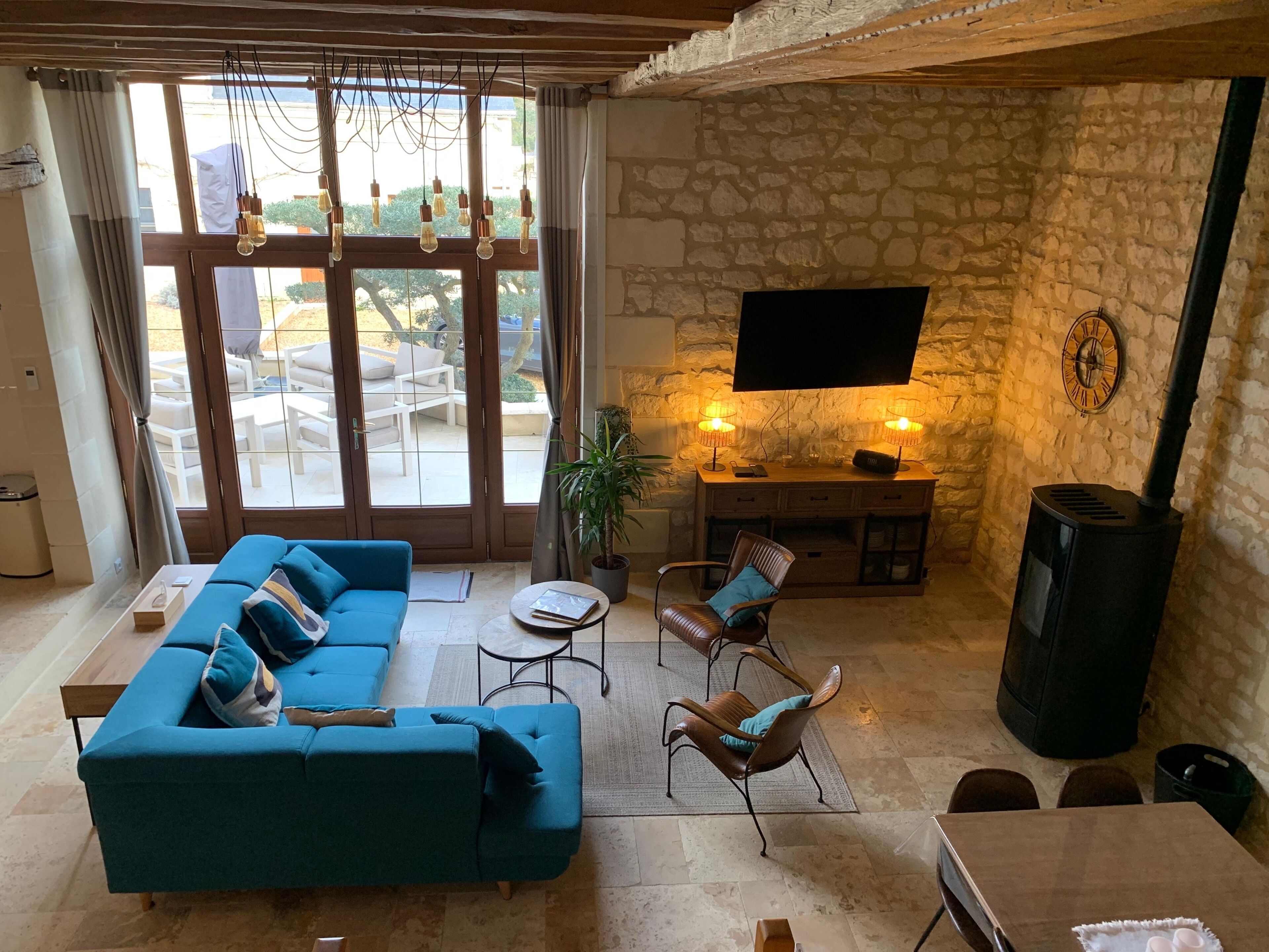 Un salon comprenant un canapé, des fauteuils, un téléviseur, une cheminée et une vue dégagée sur l’extérieur grâce à de grandes fenêtres.