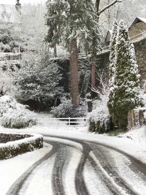 A snow-covered rural road with a winding path, surrounded by trees and a wooden fence.