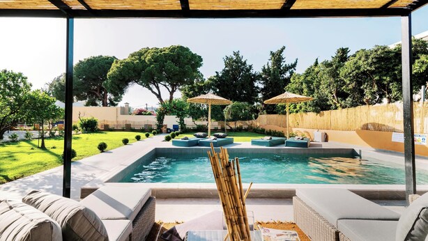 Un espace piscine agrémenté de chaises longues et de parasols, entouré de verdure et surplombé d’un ciel dégagé.