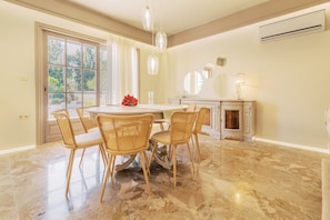 Uma sala de jantar com uma mesa redonda, quatro cadeiras de vime, um candelabro e uma lareira.