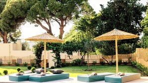 Un espace aménagé au bord de la piscine, avec des chaises longues et des parasols, entouré de verdure et délimité par une clôture.