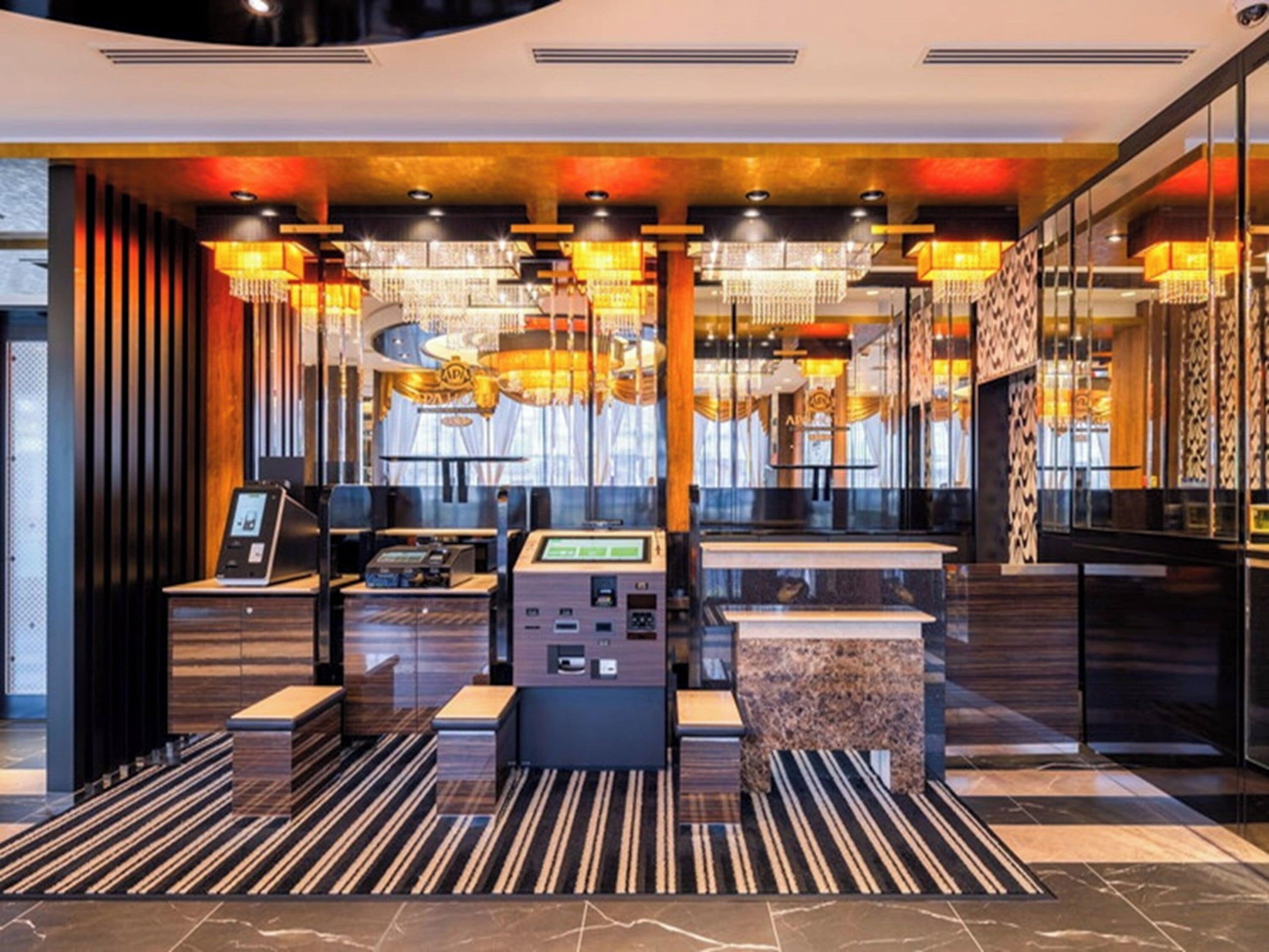 Un hall d’hôtel moderne avec un comptoir d’accueil, des bornes d’enregistrement et un lustre.