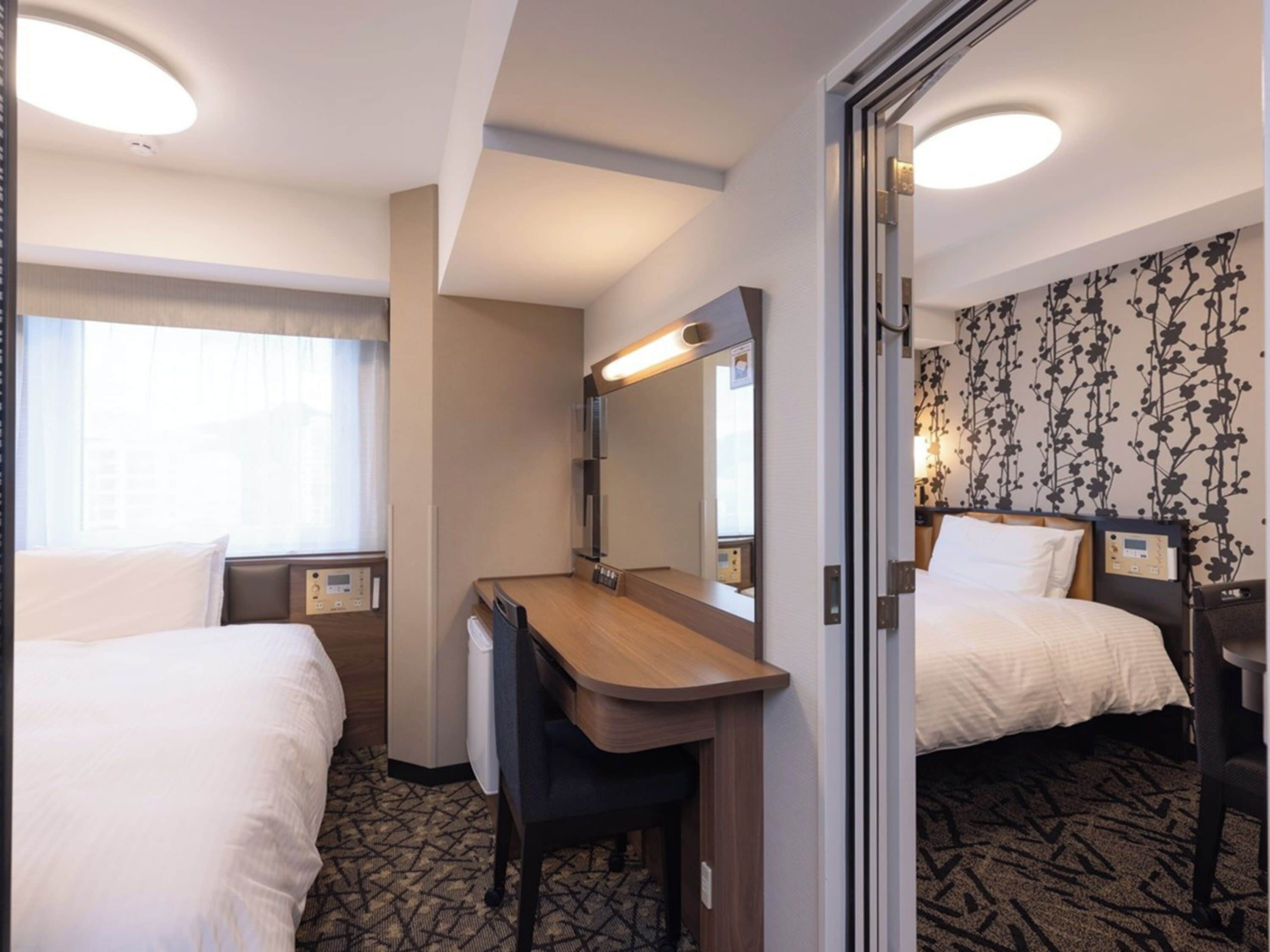 A hotel room with two beds, a desk, a mirror, and a window with curtains.