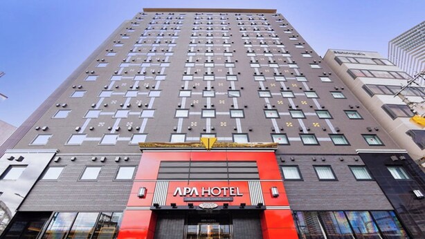 A high-rise hotel with a prominent red and black facade, multiple windows, and a visible entrance. - APA Hotel Hiroshima Ekimae Stadium Guchi (Hiroshima)