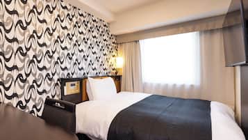 Una habitación de hotel con una cama, un escritorio, una pared con papel tapiz estampado, una ventana con cortinas y un televisor montado en la pared.