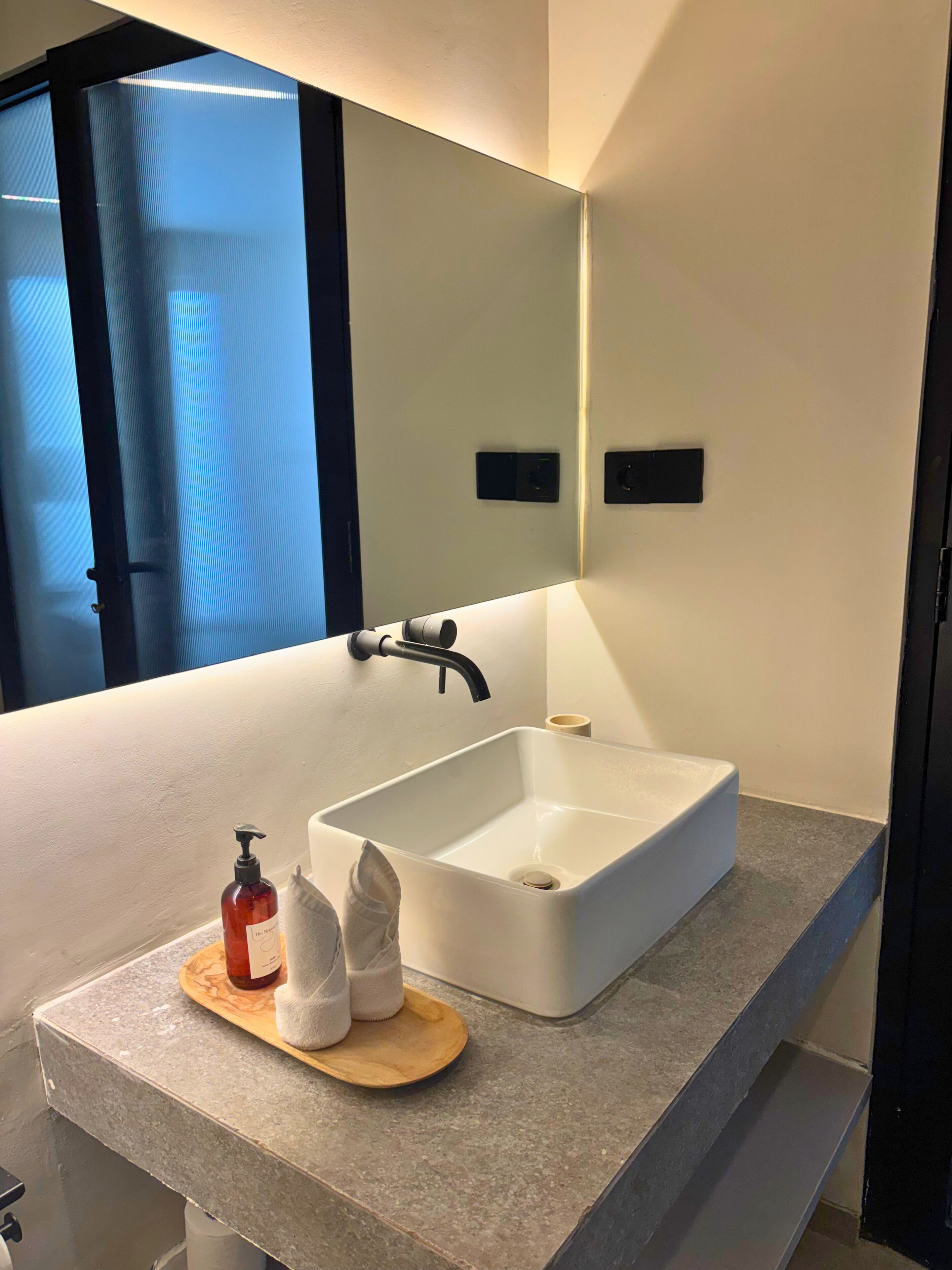 A modern bathroom with a white sink, a mirror above it, and a window with a view of a building.