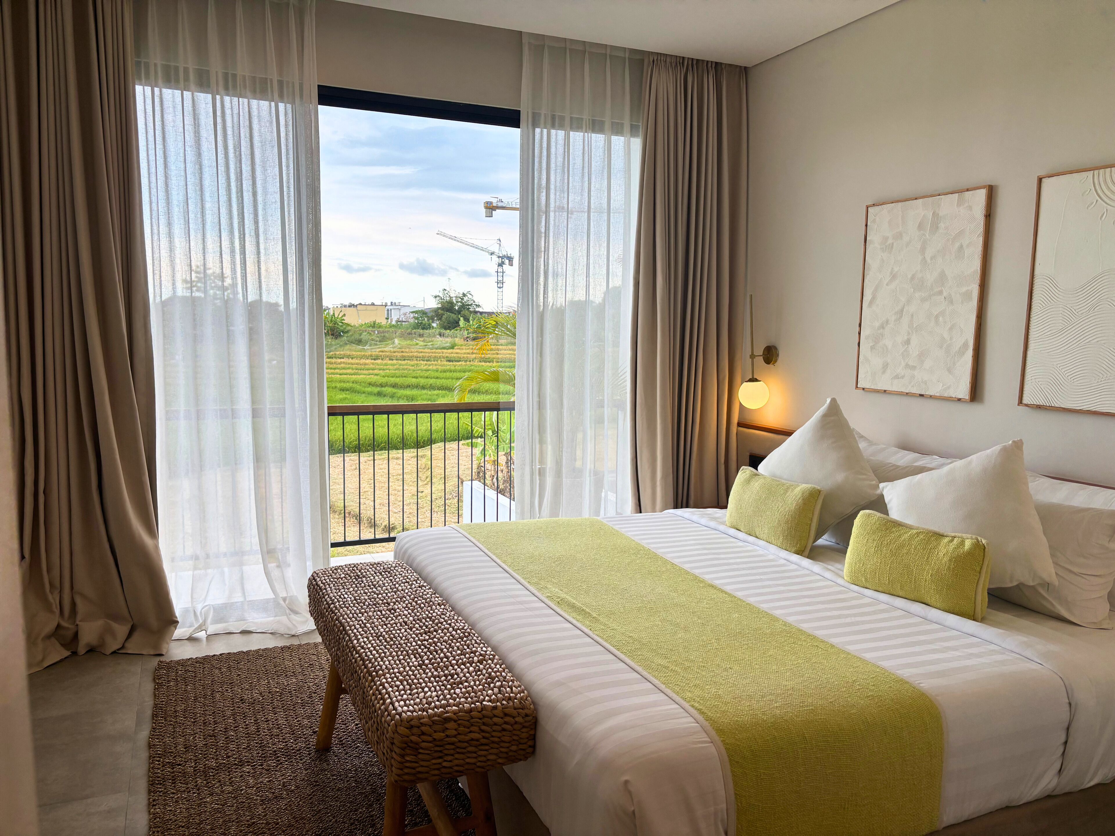 A hotel room with a bed, a bench, a view of a green field, and a balcony.
