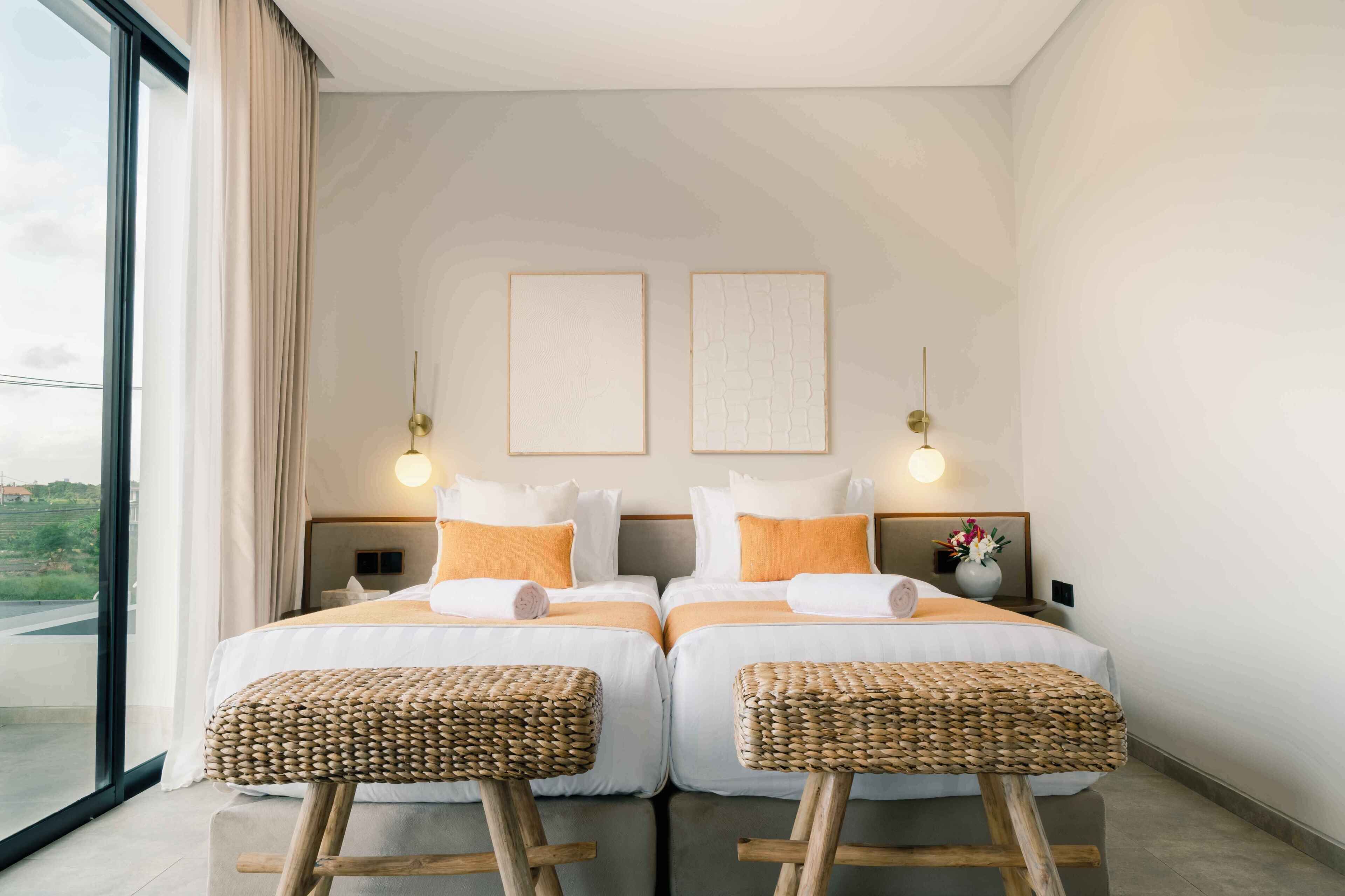 A modern hotel room with two beds, a large window, and a view of the outdoors.