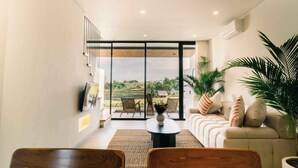 A modern living room with a sofa, coffee table, and chairs, large sliding glass doors leading to a balcony with a view of the countryside. - The Menuai Bali Villas Canggu (Canggu)
