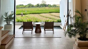A modern interior with a view of a rice field, a dining area with chairs and a table, and a sofa. - The Menuai Bali Villas Canggu (Canggu)