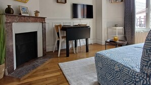 Una sala moderna con chimenea, comedor, televisor de pantalla plana montado en la pared y cama con ropa de cama estampada.