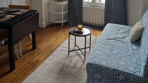 Una sala de estar con sofá, mesa de centro, televisor, una mesita auxiliar y una ventana con cortinas.