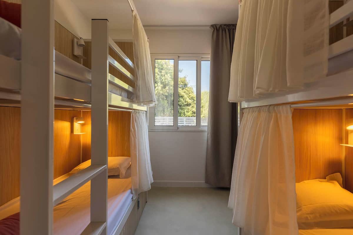 Ein Schlafsaalzimmer mit Etagenbetten, einem Fenster mit Blick auf Bäume und einem Vorhang.