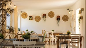 Een eethoek met meerdere houten tafels en stoelen, omringd door gevlochten manden en wandplanten.
