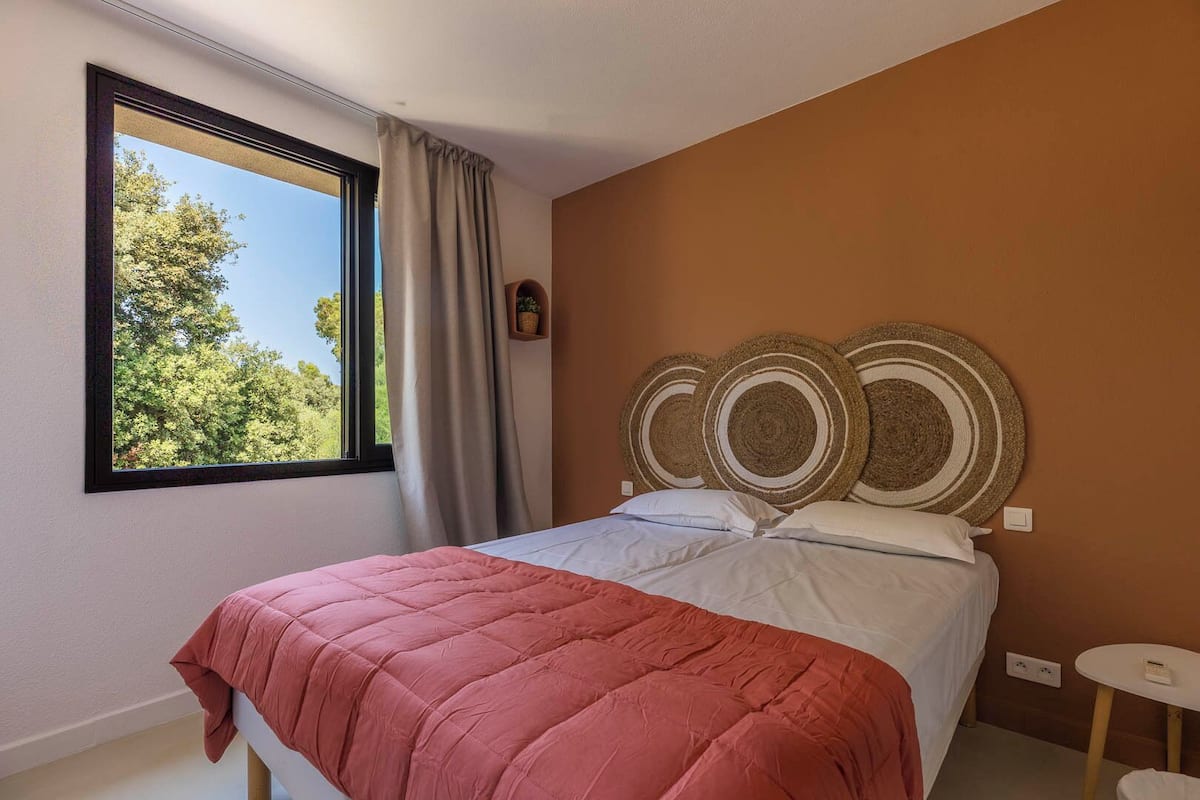 Ein Schlafzimmer mit einem Bett, einem Fenster mit Vorhängen, einem an der Wand befestigten Regal mit einer Pflanze und einer runden Wanddekoration.