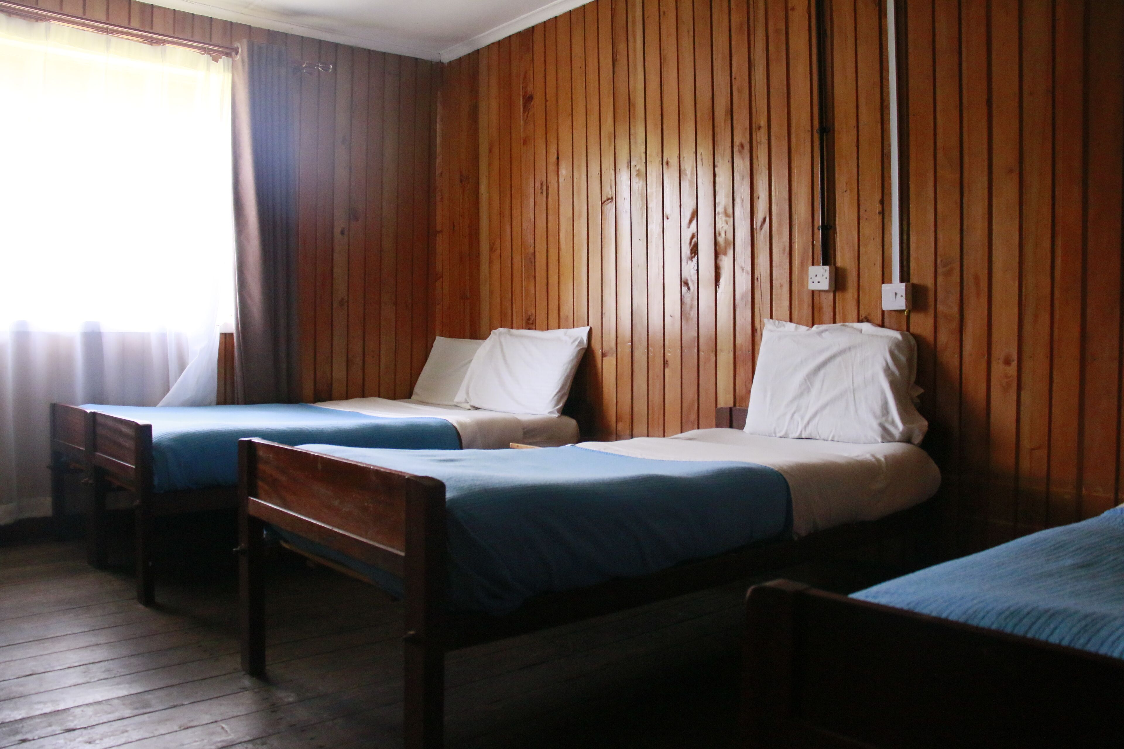 A room with two wooden beds, a wooden floor, and a window with curtains.