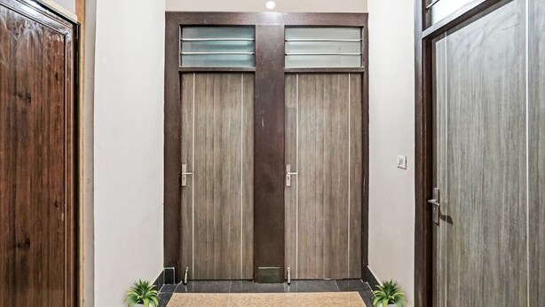 A hallway with two wooden doors, a light fixture, and a small rug. - Vishen Residency (Greater Noida)